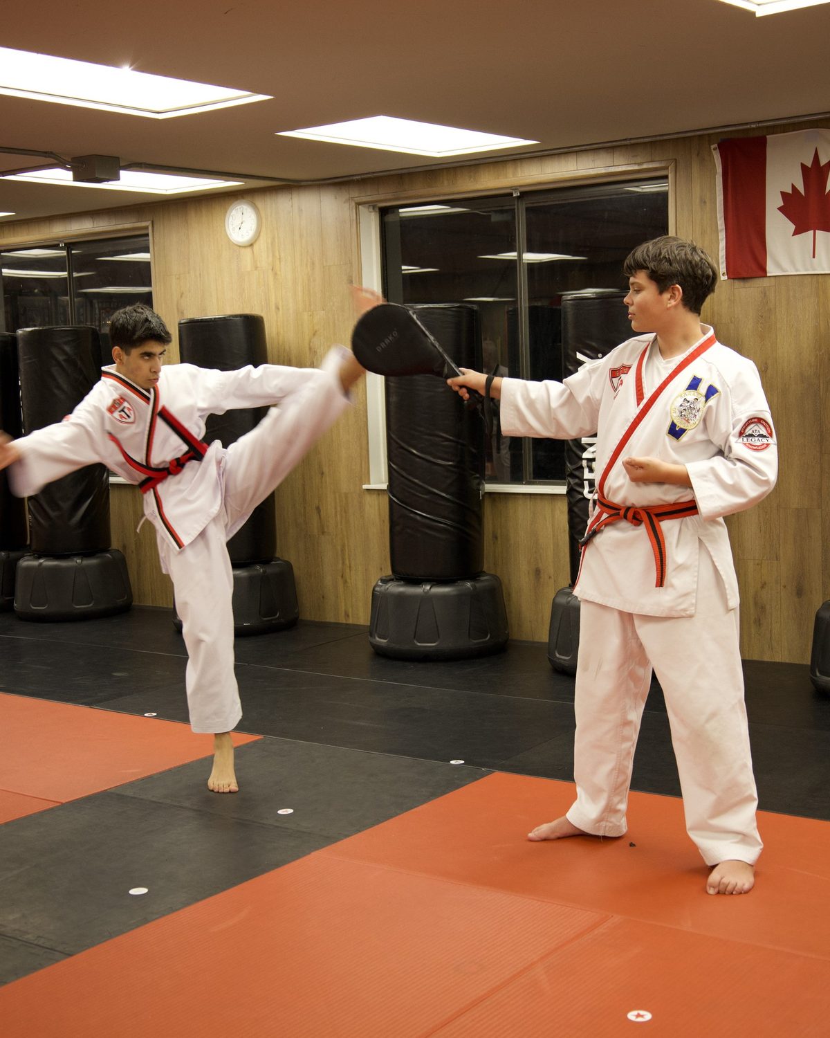 A student throwing a high kick into a target pad held by a partner, martial arts south surrey at Kingdom Athletics