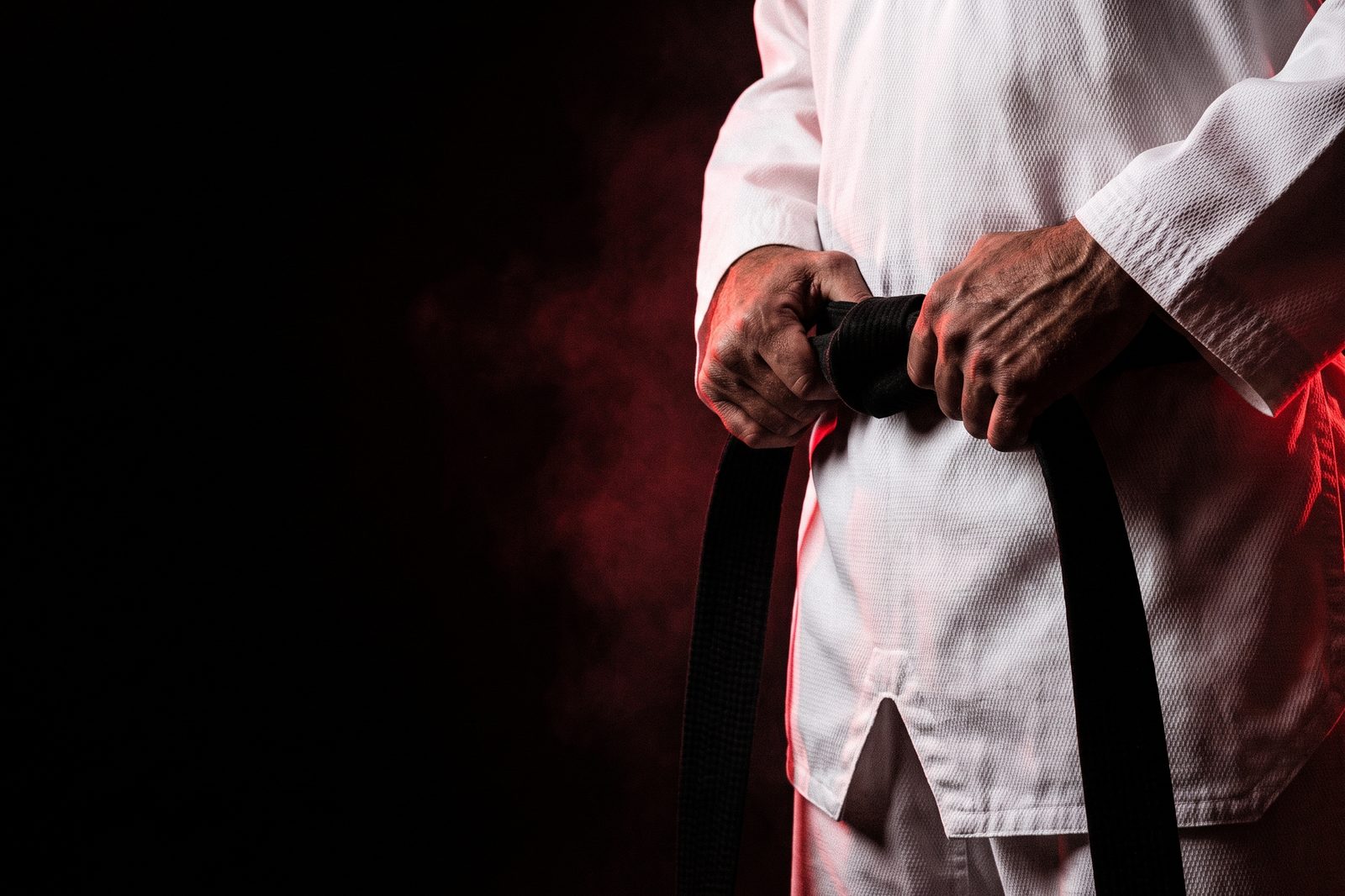 Hands tying a black belt around a white taekwondo uniform