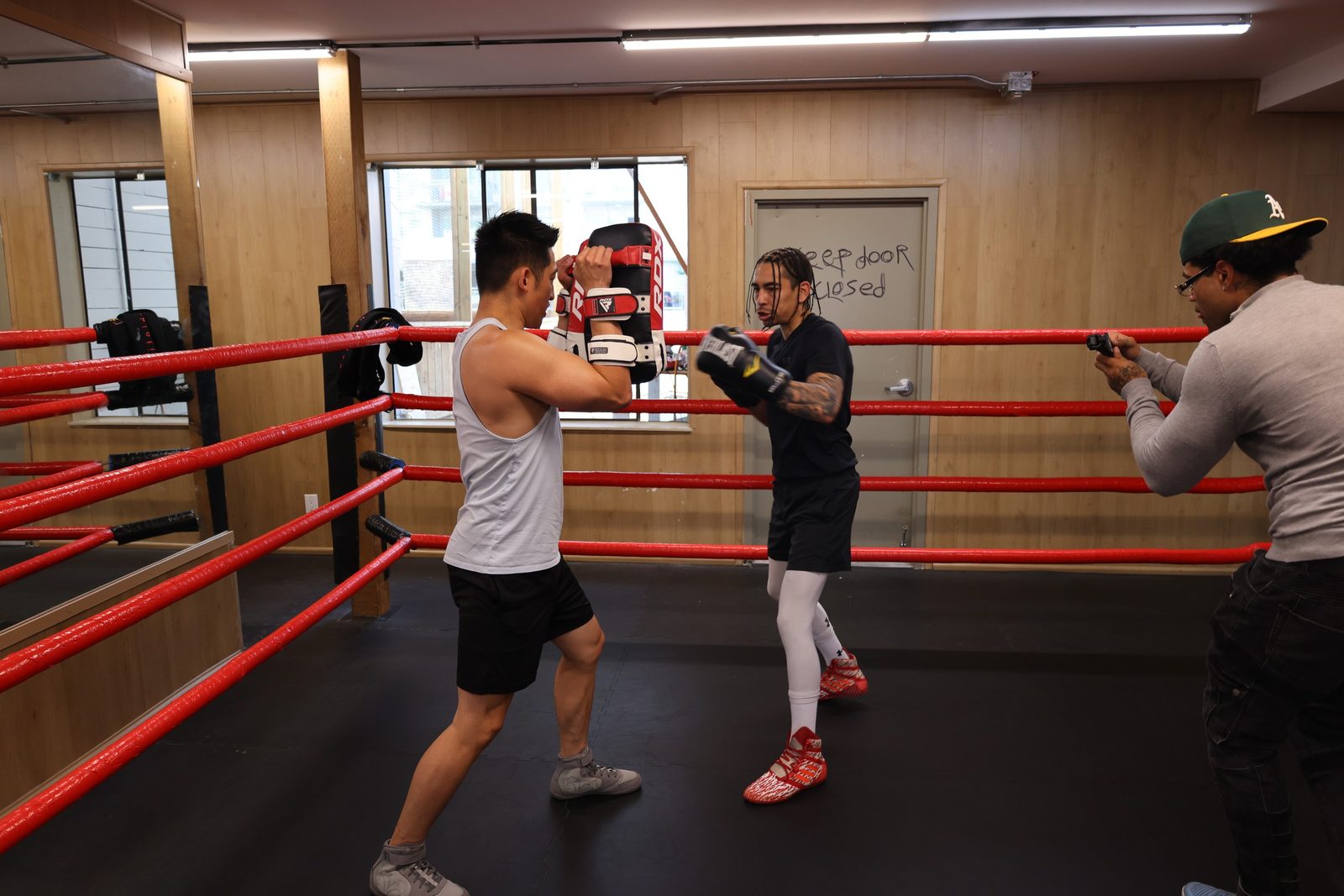 A coach holding pads while a member throws a combination at Kingdom Athletics